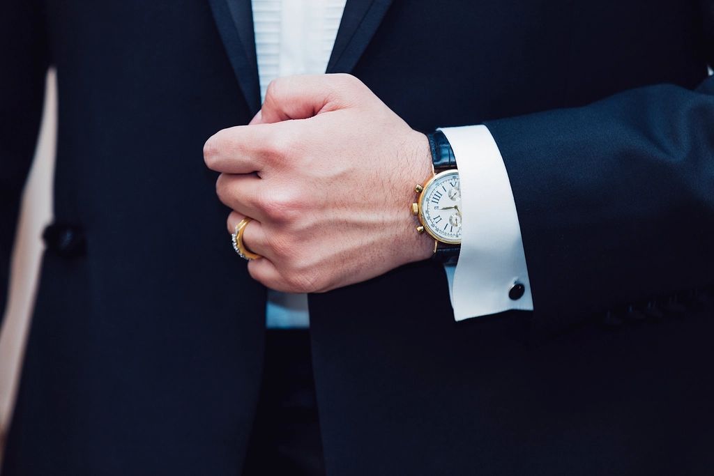 Close-up of a man in a dark suit adjusting a cufflink, with a gold watch on his wrist