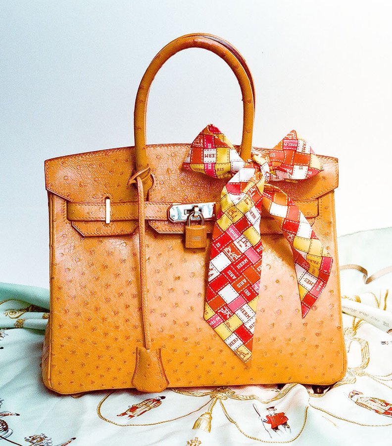 An orange ostrich-leather Birkin bag with a silk scarf tied to the handle