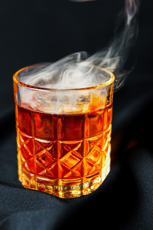 A crystal tumbler of whiskey with smoke rising from it